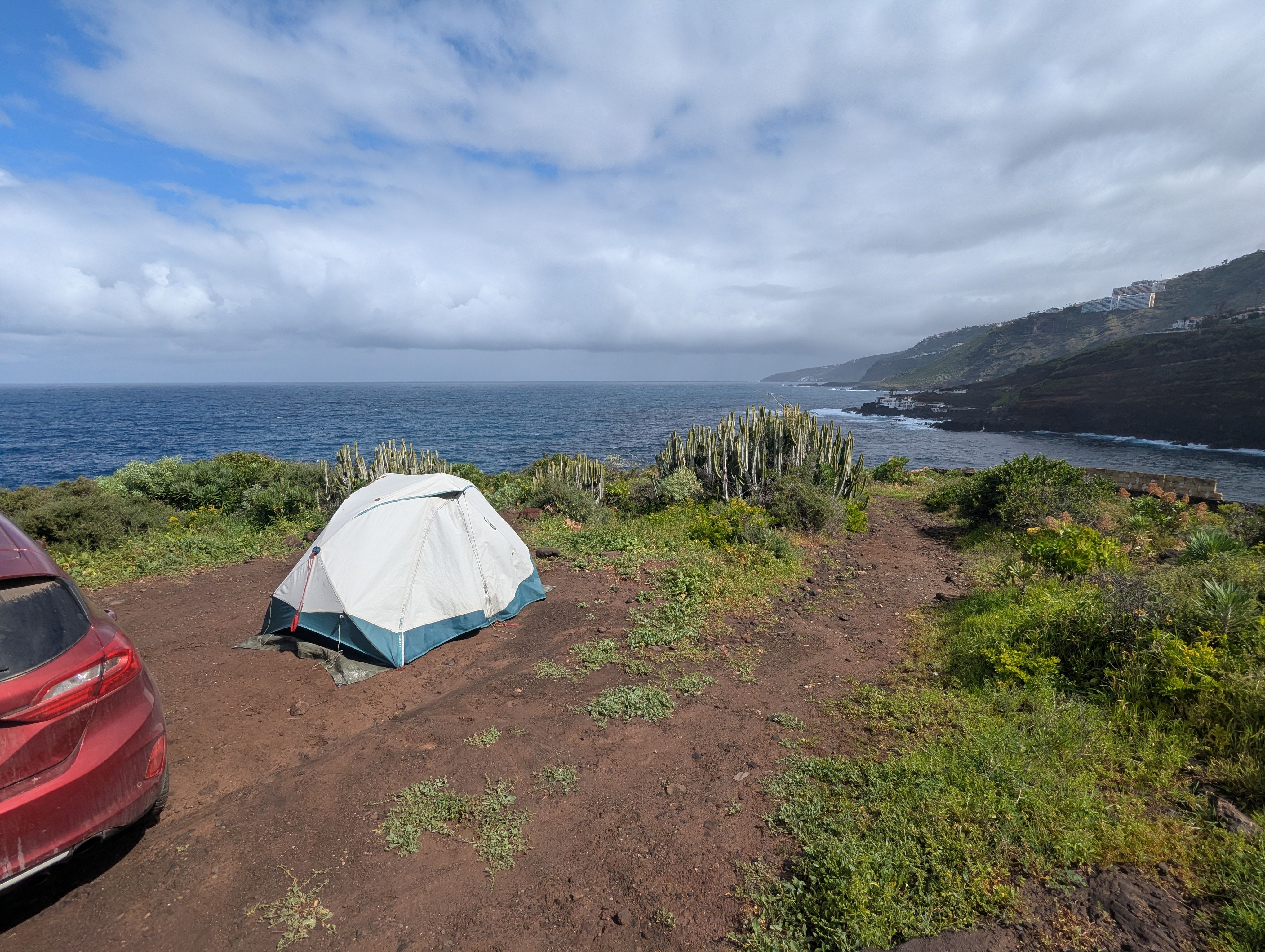 Luca (Vivi)'s Decathlon 2 seconds Easy tent pitched next to his red car, on a cliff on the sea, with the sea, sky and coastline in the background.